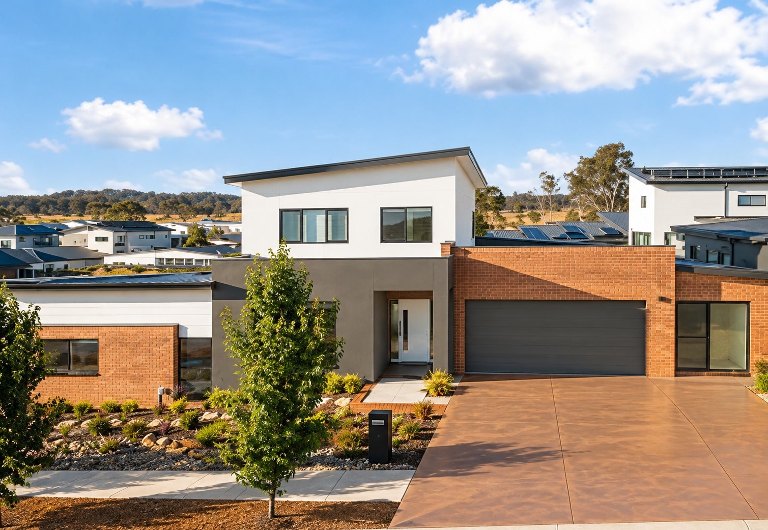 Terracotta-coloured concrete driveway leading to the garage of a new brick and render home in a Canberra estate