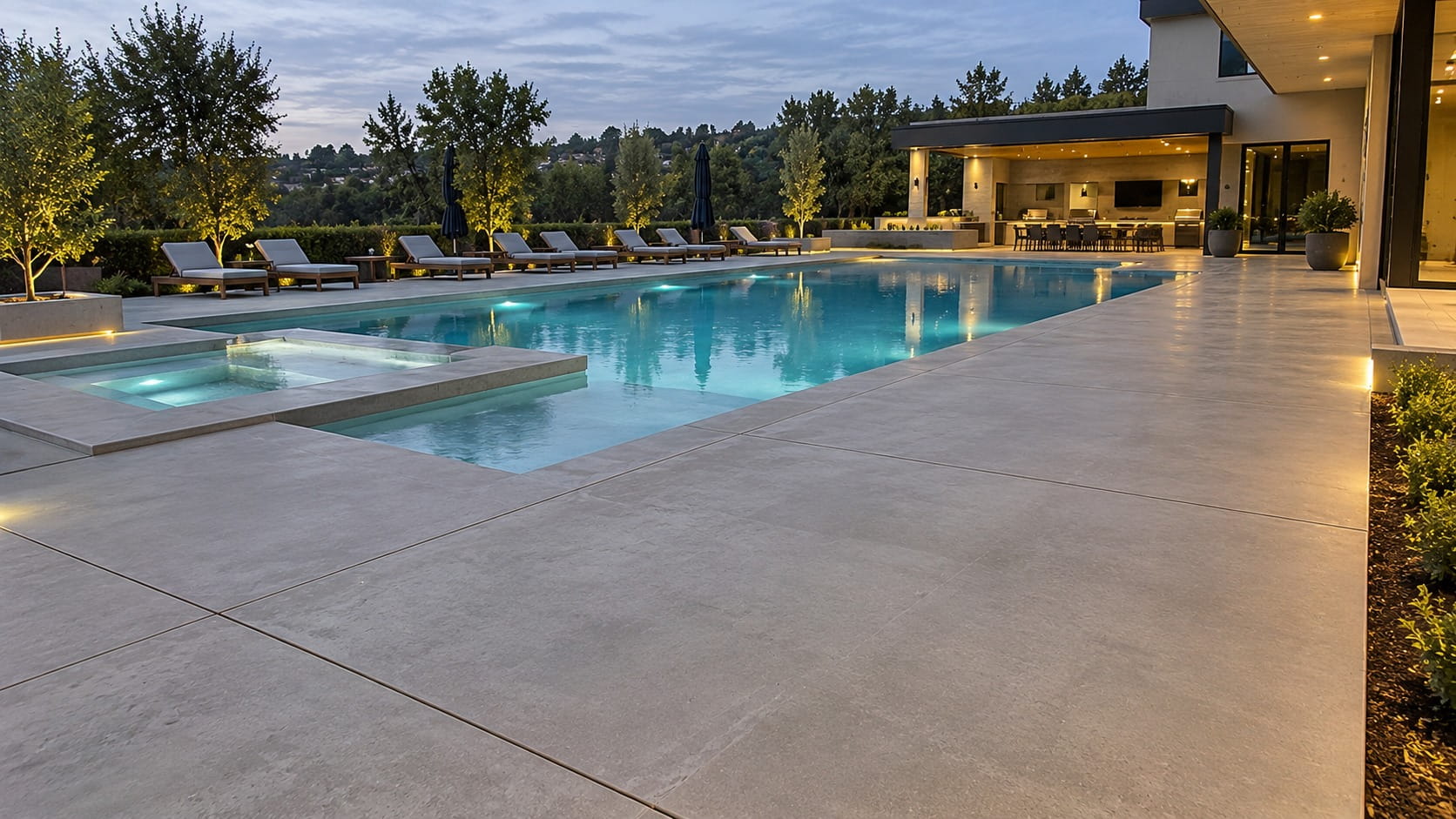 Wide concrete pool surround with saw-cut joints around a lit pool and spa at a Canberra home at dusk
