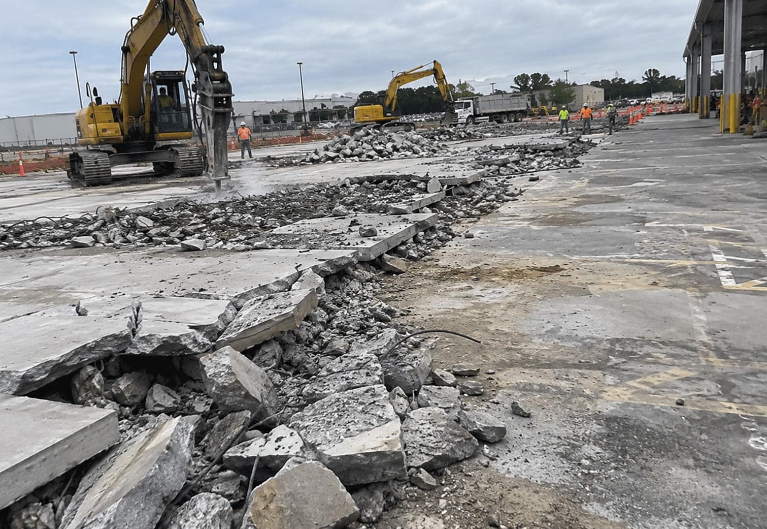 Excavators with hydraulic breakers removing an old concrete car park, with broken slabs piled in the foreground in Canberra