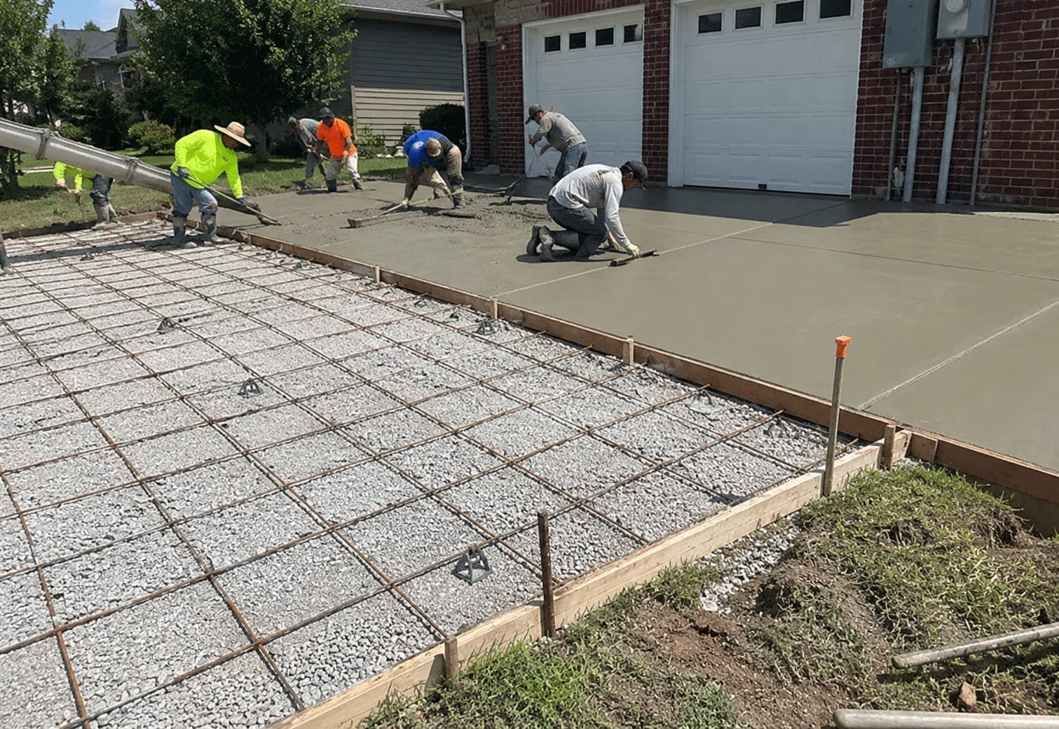 Concrete crew placing and screeding a fresh driveway surface over steel mesh in front of a double garage in Canberra