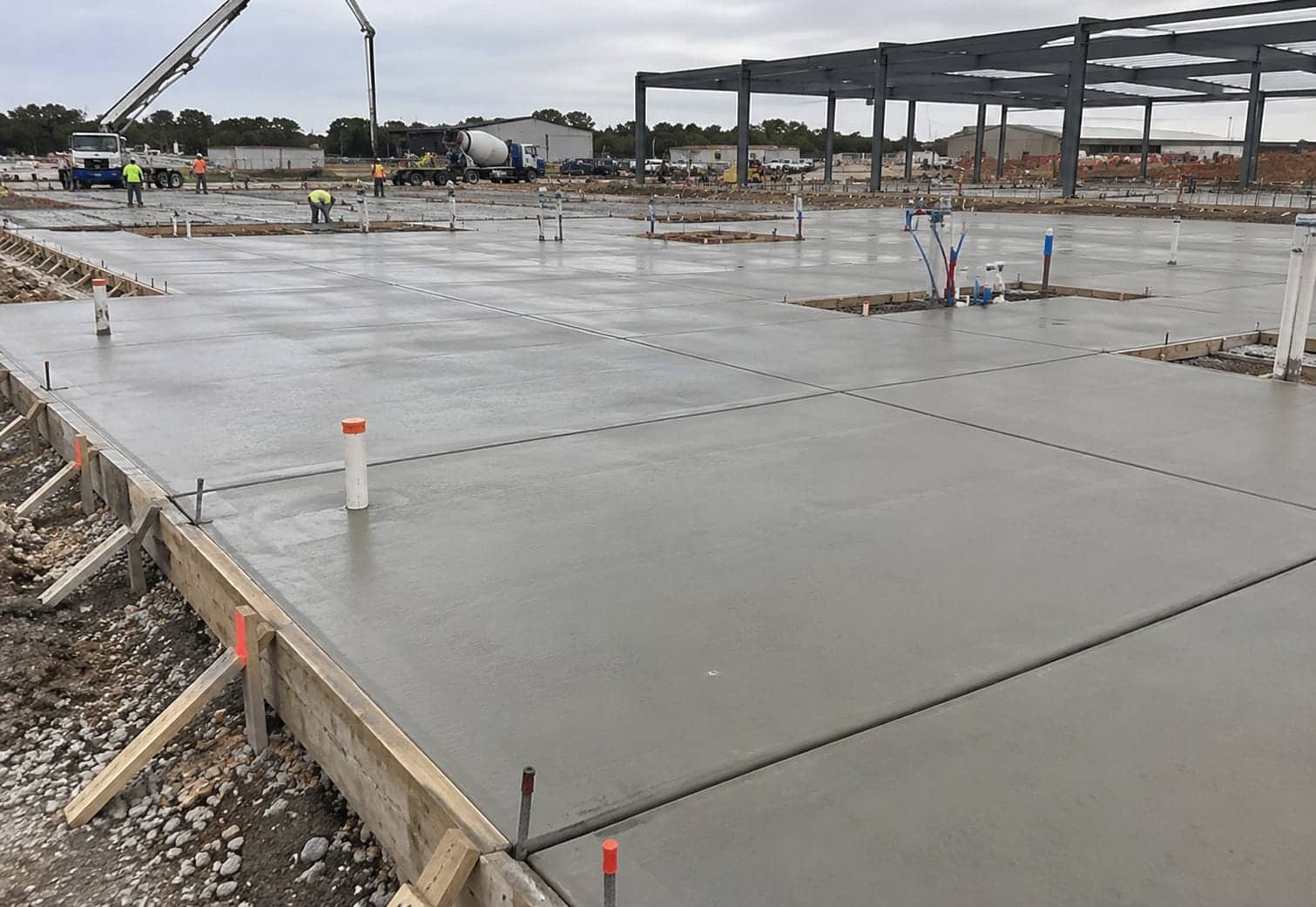 Freshly poured and jointed concrete slab with service risers and a concrete pump working on a Canberra commercial build