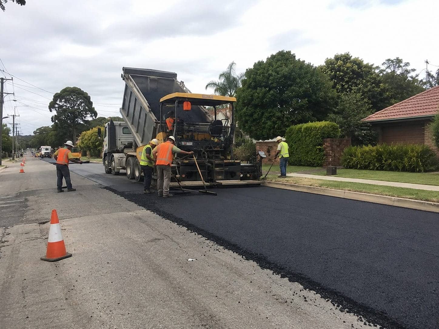 Road crew in hi-vis laying a fresh asphalt surface from a paver and tipper truck on a suburban Canberra street