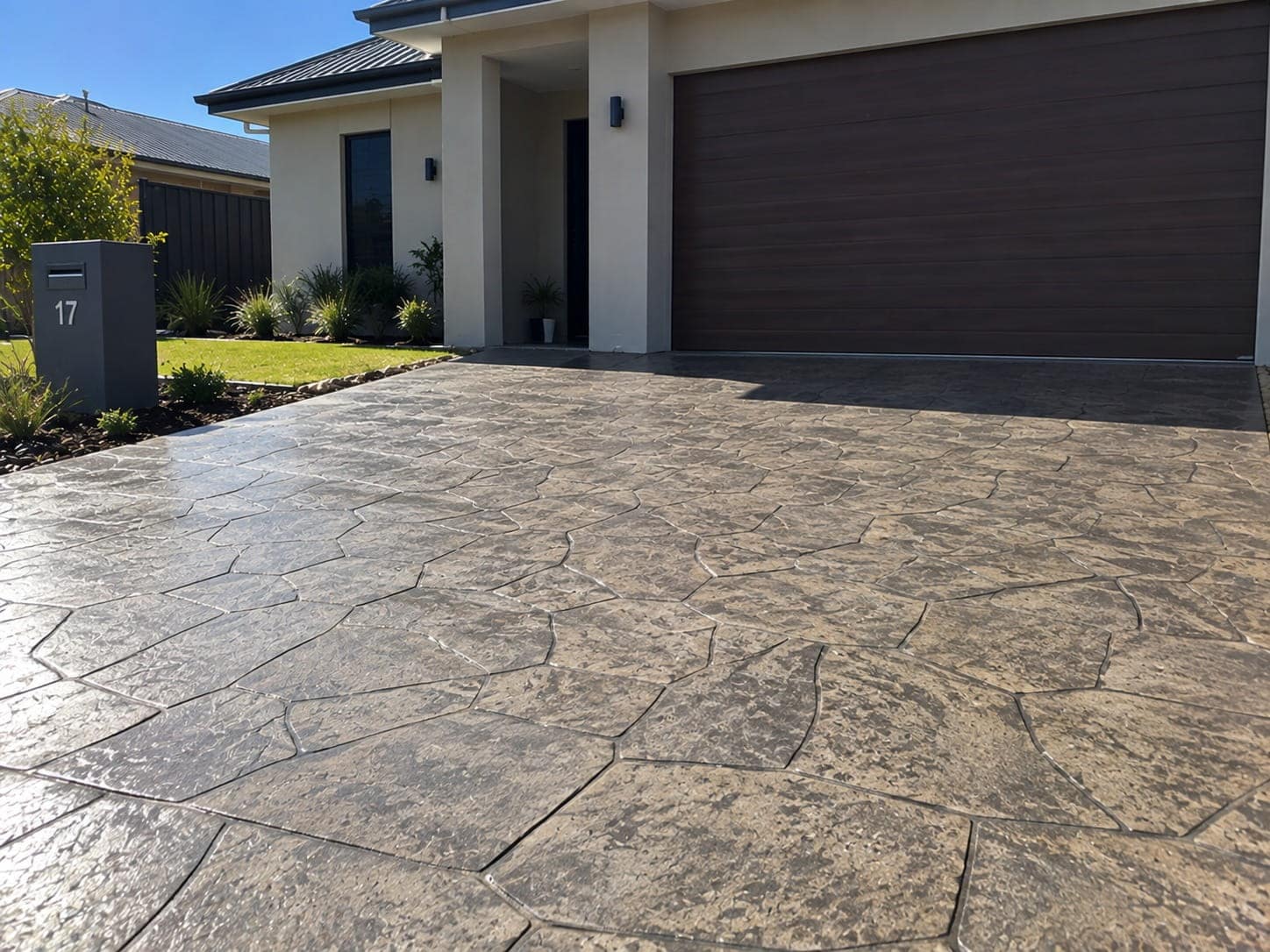 Ashlar-pattern stamped concrete driveway leading to a dark garage door in Canberra