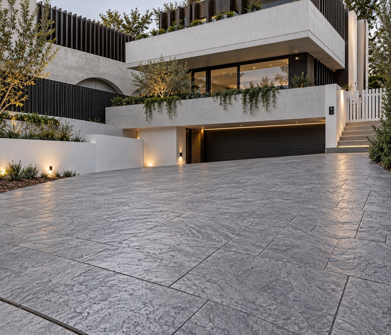 Grey slate-textured stamped concrete driveway sloping up to the garage of a contemporary Canberra home at dusk